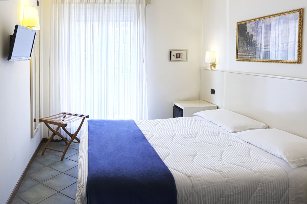A hotel room with a bed, a nightstand, a lamp, a painting, and a window with curtains.