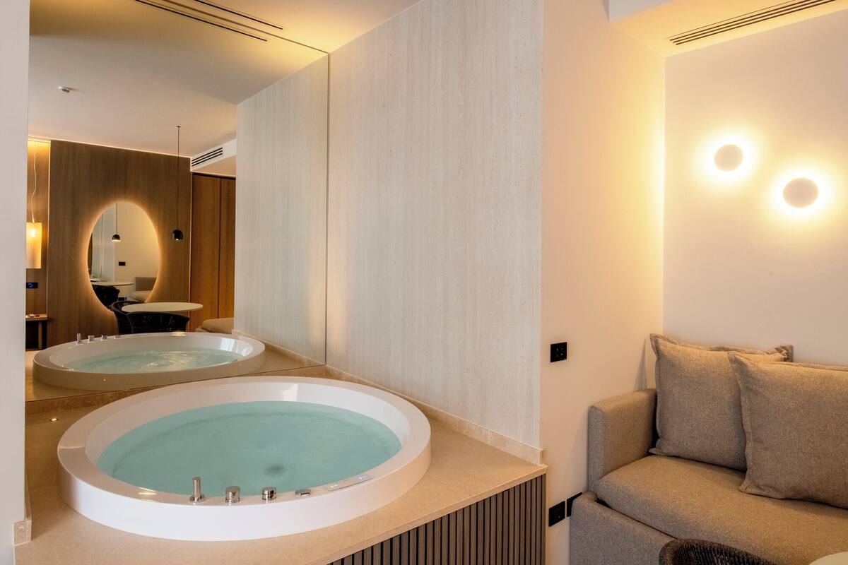 A modern bathroom with two large tubs, a mirror, and a sofa.