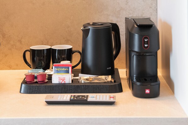 A coffee station with two black mugs, a black electric kettle, a coffee maker, and a remote control. - International Hotel & Suite (San Benedetto del Tronto)