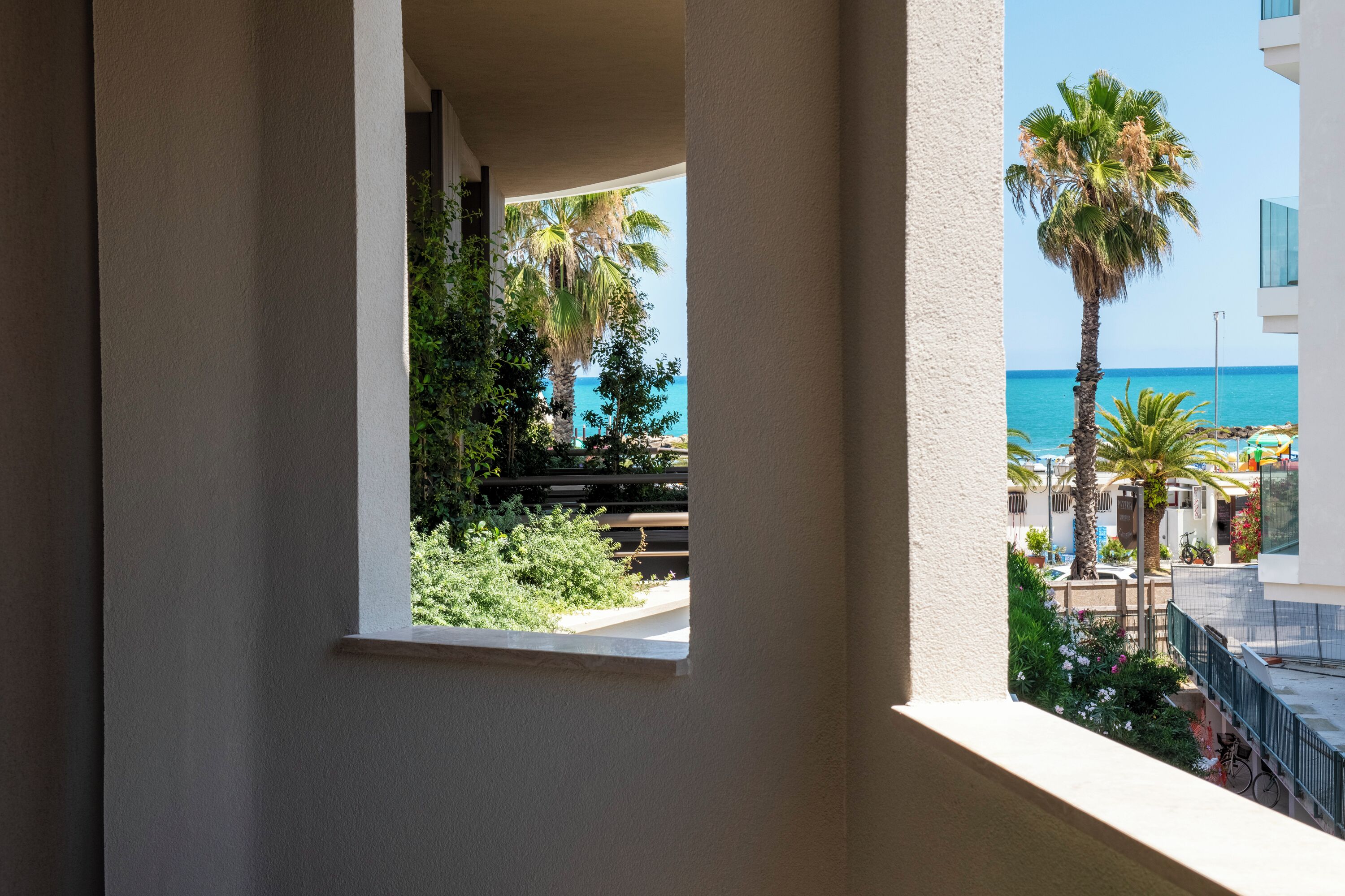Ein Balkon mit Blick auf eine Palme und ein Gebäude gegenüber.