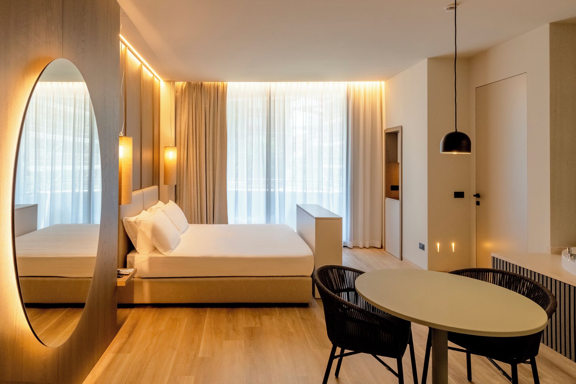 A modern hotel room with a bed, a dining area, and a large mirror.