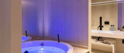 A modern bathroom with a large, illuminated bathtub, a vanity with a mirror, and a bench under the sink.