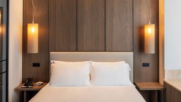 Una habitación de hotel con una cama grande, dos mesitas de noche y dos lámparas fijadas a la pared.