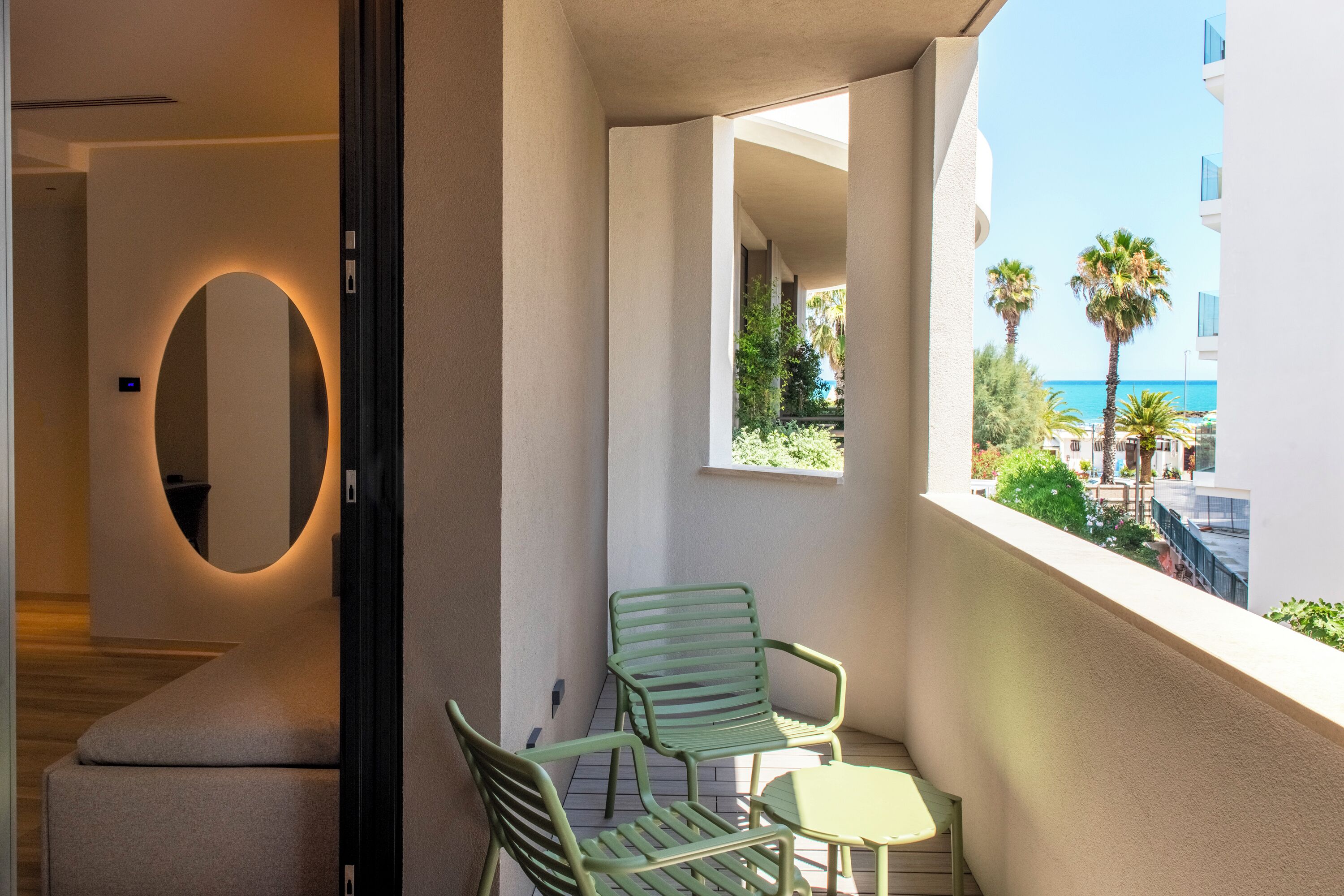 A balcony with a view of the sea, a small table, two chairs, and a mirror.