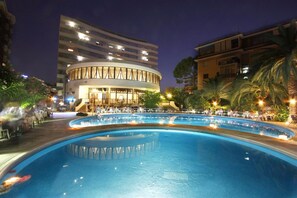 A hotel with a circular pool, a restaurant, and a modern building in the background.