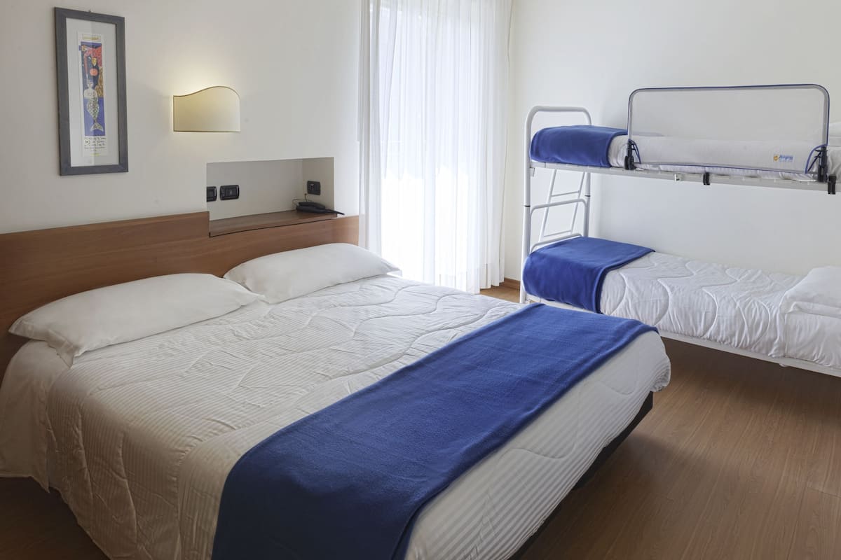 A hotel room with a large bed, a smaller bed, a bedside table, a wall-mounted light, and a window with curtains.