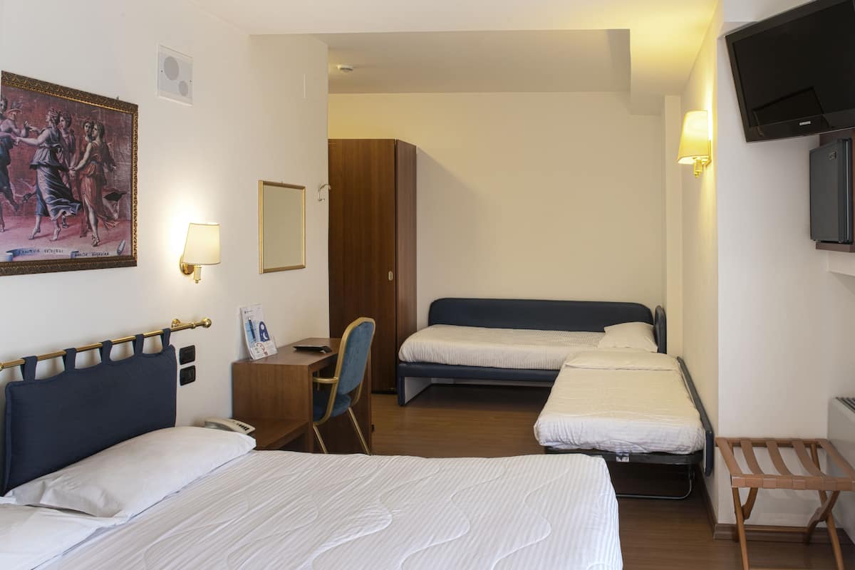 A hotel room with three beds, a desk, a chair, a TV, and a painting on the wall.