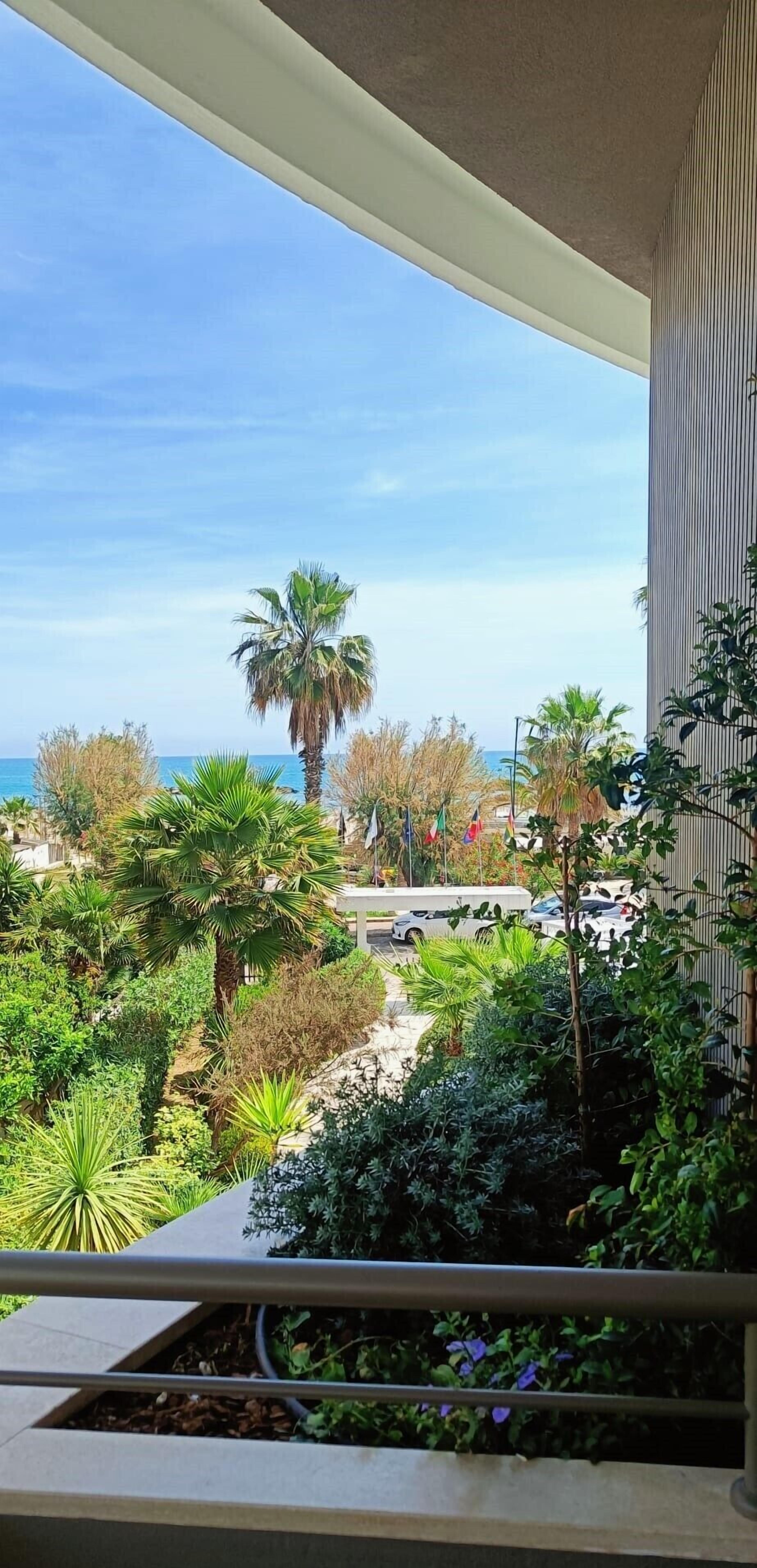 A balcony with a view of a landscaped garden, palm trees, and a building in the background.
