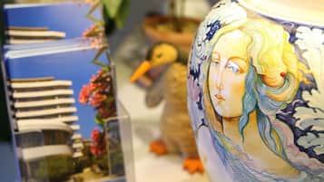 Un vaso di ceramica decorativo con un volto dipinto, una teca in vetro trasparente con un modellino di edificio e un piccolo giocattolo a forma di anatra.