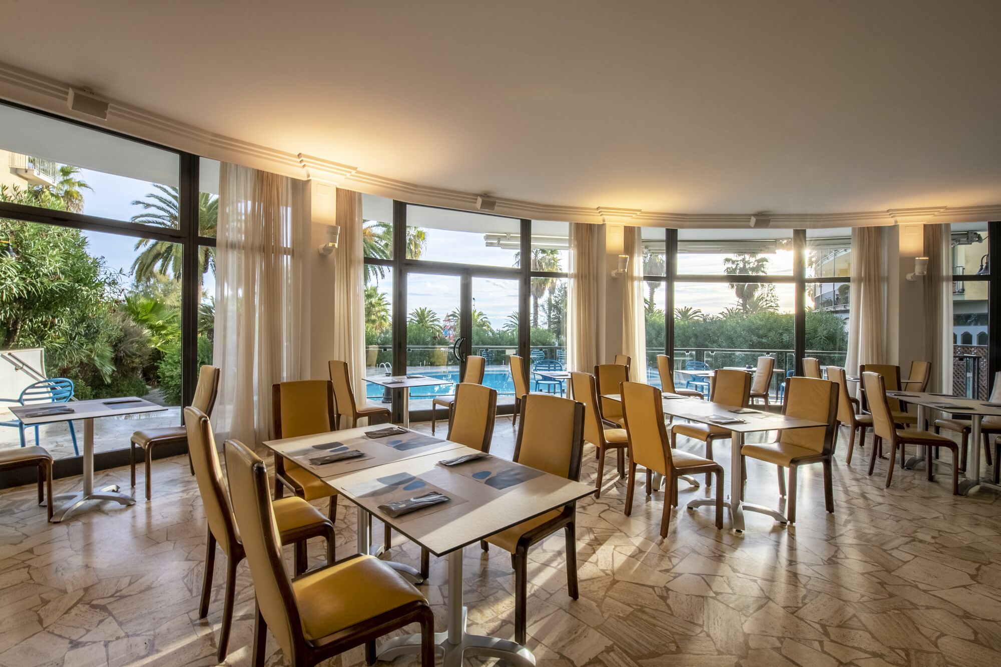 Un'ampia sala da pranzo con grandi finestre, vista piscina e un moderno design d'interni.
