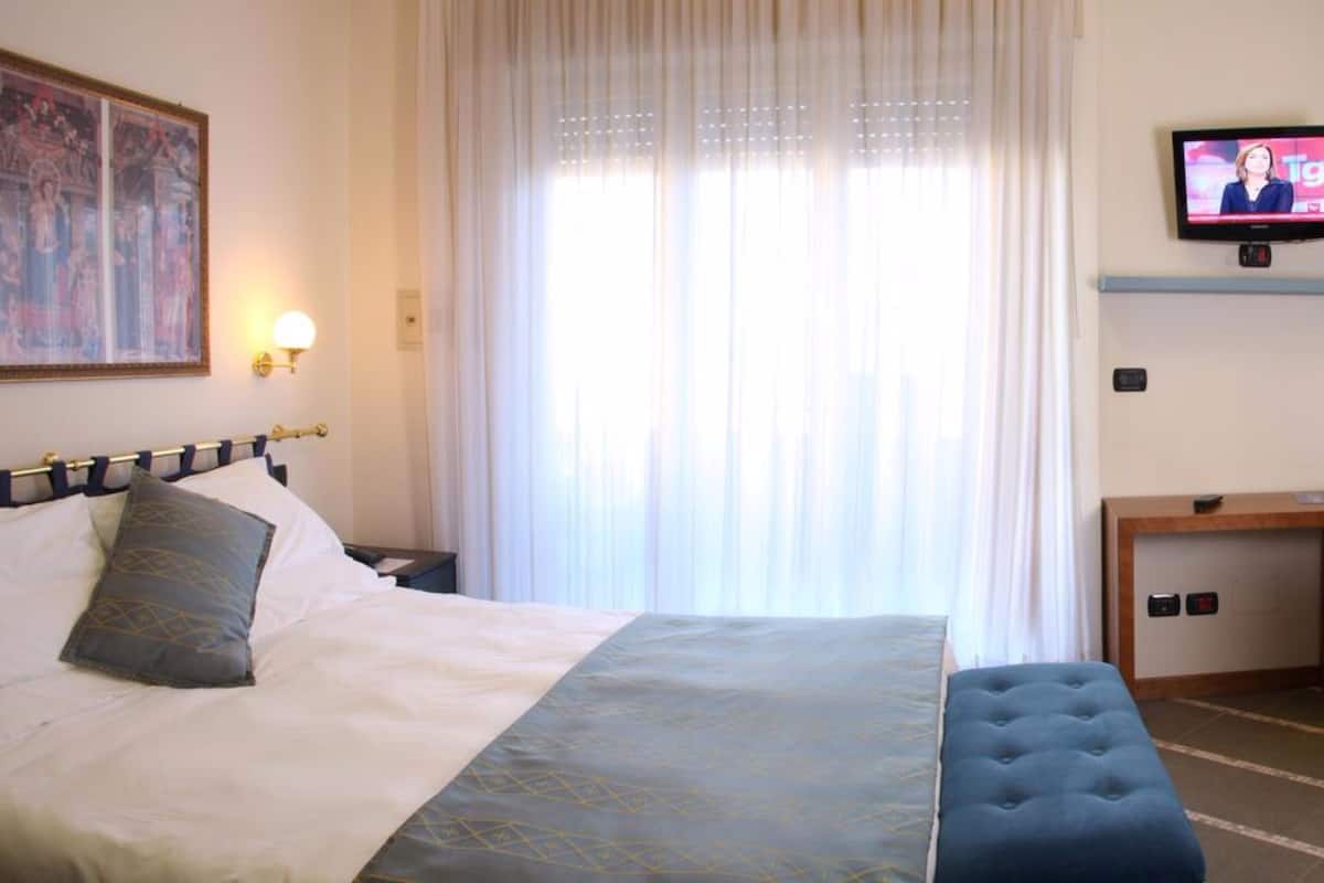 A hotel room with a bed, a television, a desk, a chair, and a mirror.