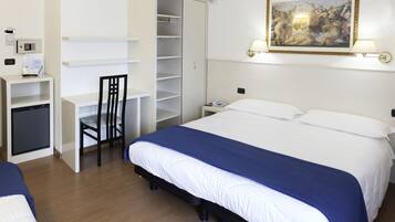A hotel room with a bed, a desk with a chair, a wardrobe, a bedside table with a lamp, and a painting on the wall.