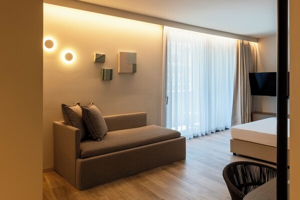 Una habitación de hotel moderna con sofá, televisión de pantalla plana y un amplio ventanal con cortinas.