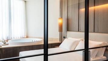 Een moderne hotelkamer met een groot bed, een inbouww badkuip en een groot raam met gordijnen.