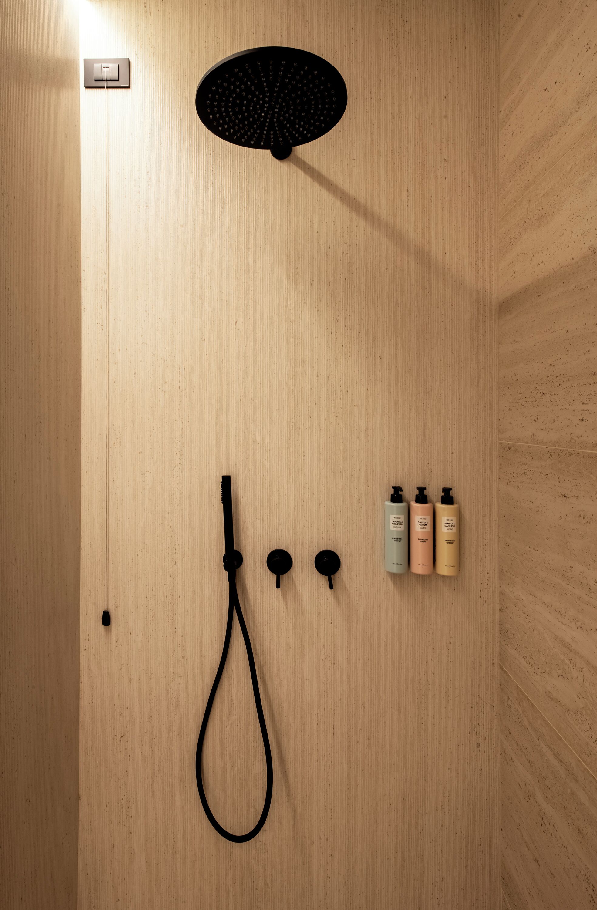 A shower with a handheld showerhead, a wall-mounted control panel, and three bottles of shampoo.