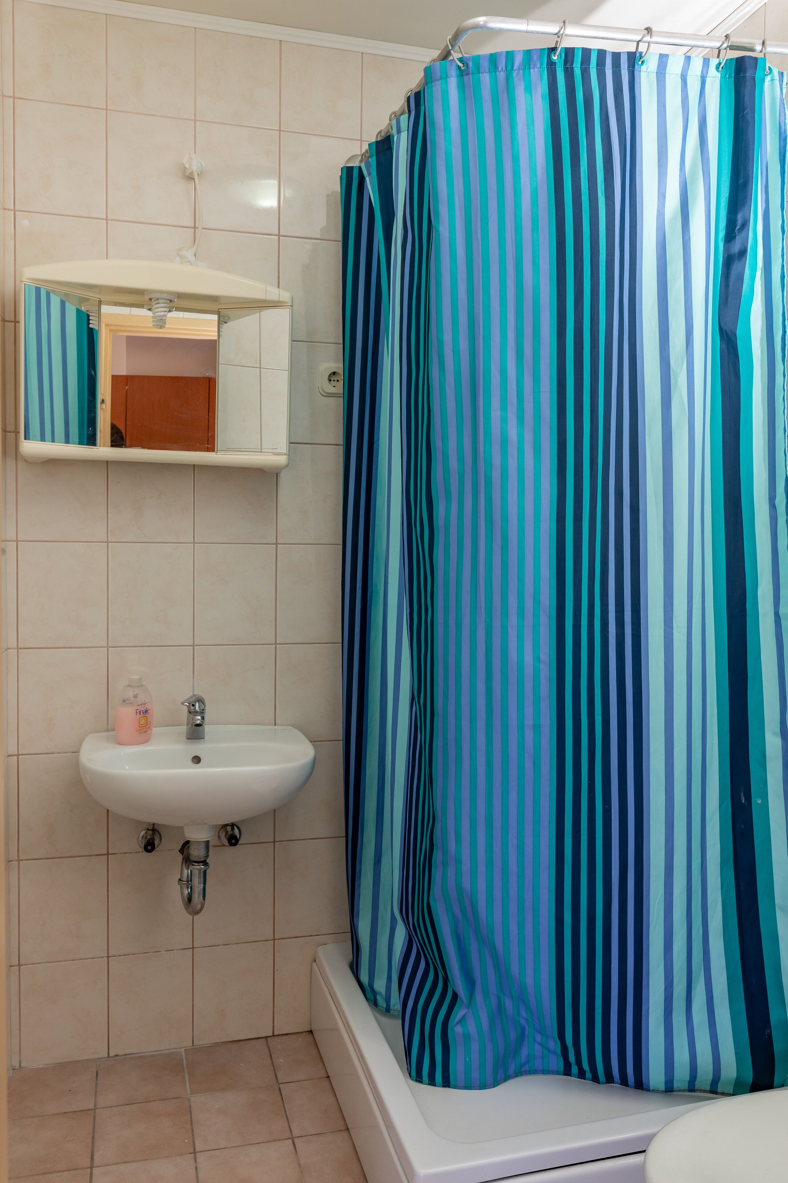 Een badkamer met een witte wastafel, een spiegel en een douchegordijn met verticale strepen.