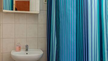 Een badkamer met een witte wastafel, een spiegel en een douchegordijn met verticale strepen.