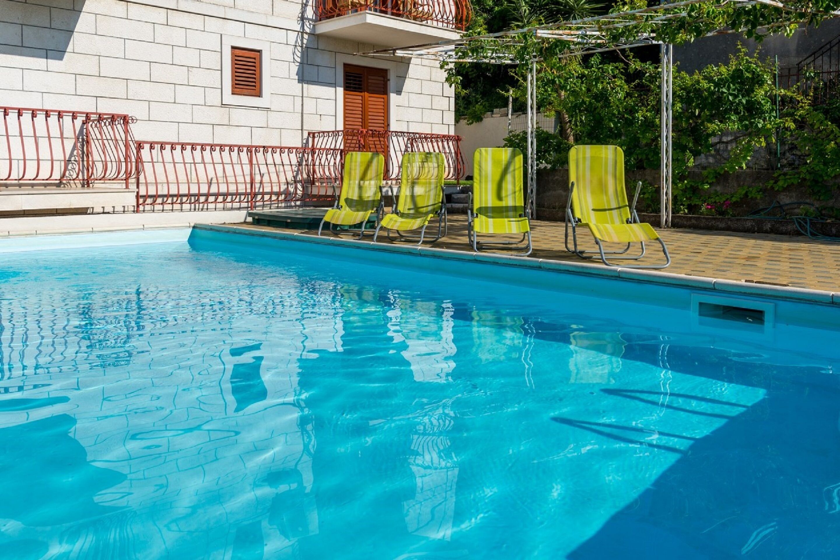Une piscine à l’eau d’un bleu cristallin, entourée d’un bâtiment blanc doté d’un balcon et d’une clôture en métal rouge.