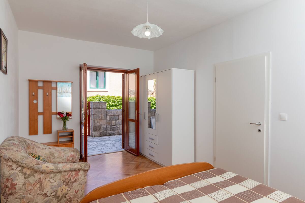 A bedroom with a bed, a wardrobe, a chair, and a door leading to an outdoor area.