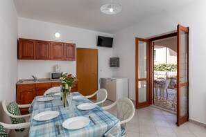 Un comedor con una mesa dispuesta para cuatro, armarios de madera, un microondas, un refrigerador pequeño y un televisor en la pared.