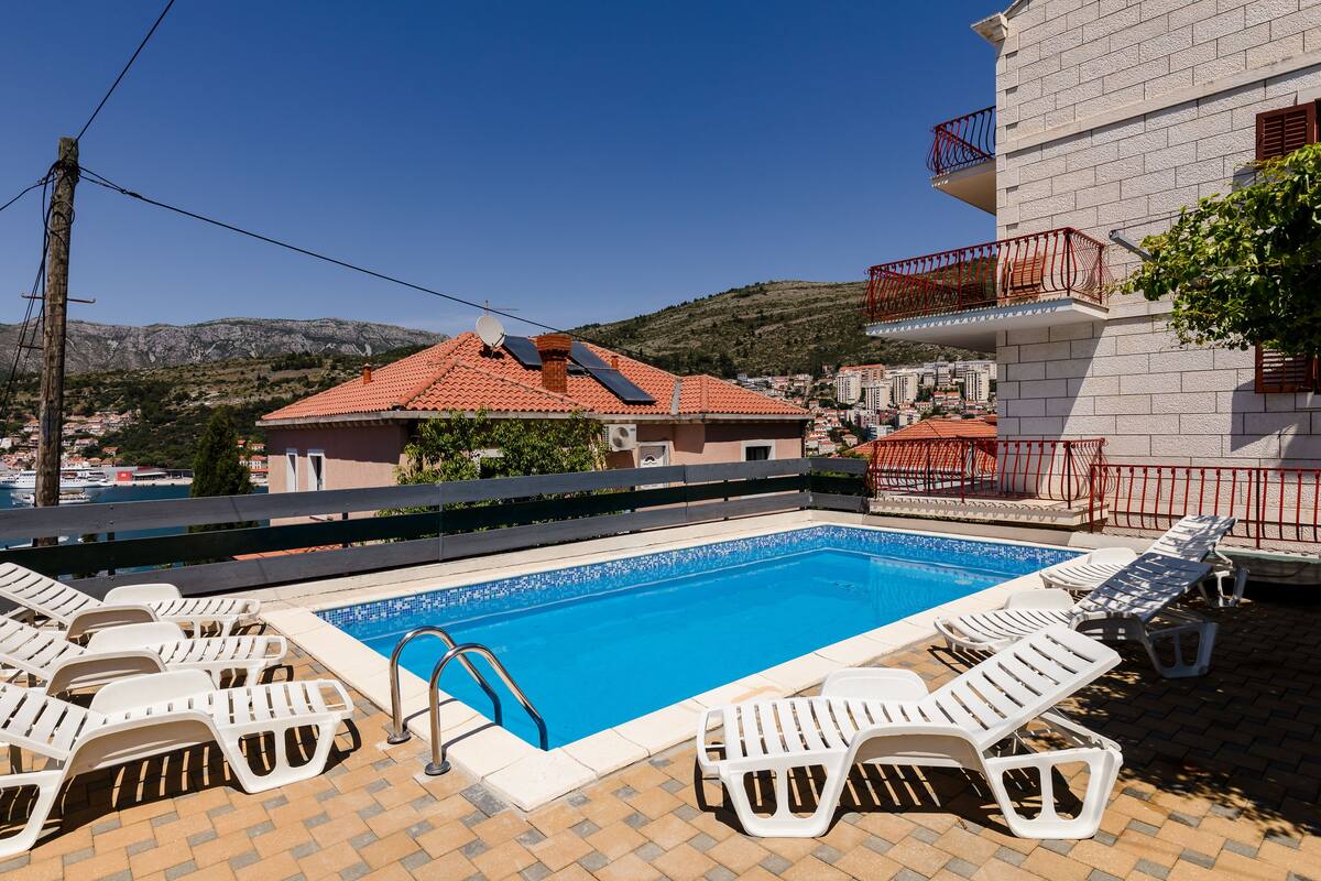 A swimming pool with sun loungers and a view of a mountainous landscape.