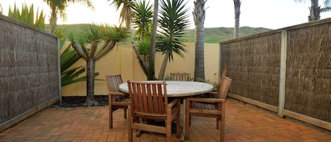 An outdoor patio with a round table and chairs, surrounded by palm trees and a brick floor.
