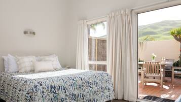 Un dormitorio con cama, ventana y vista a un patio con mobiliario exterior.