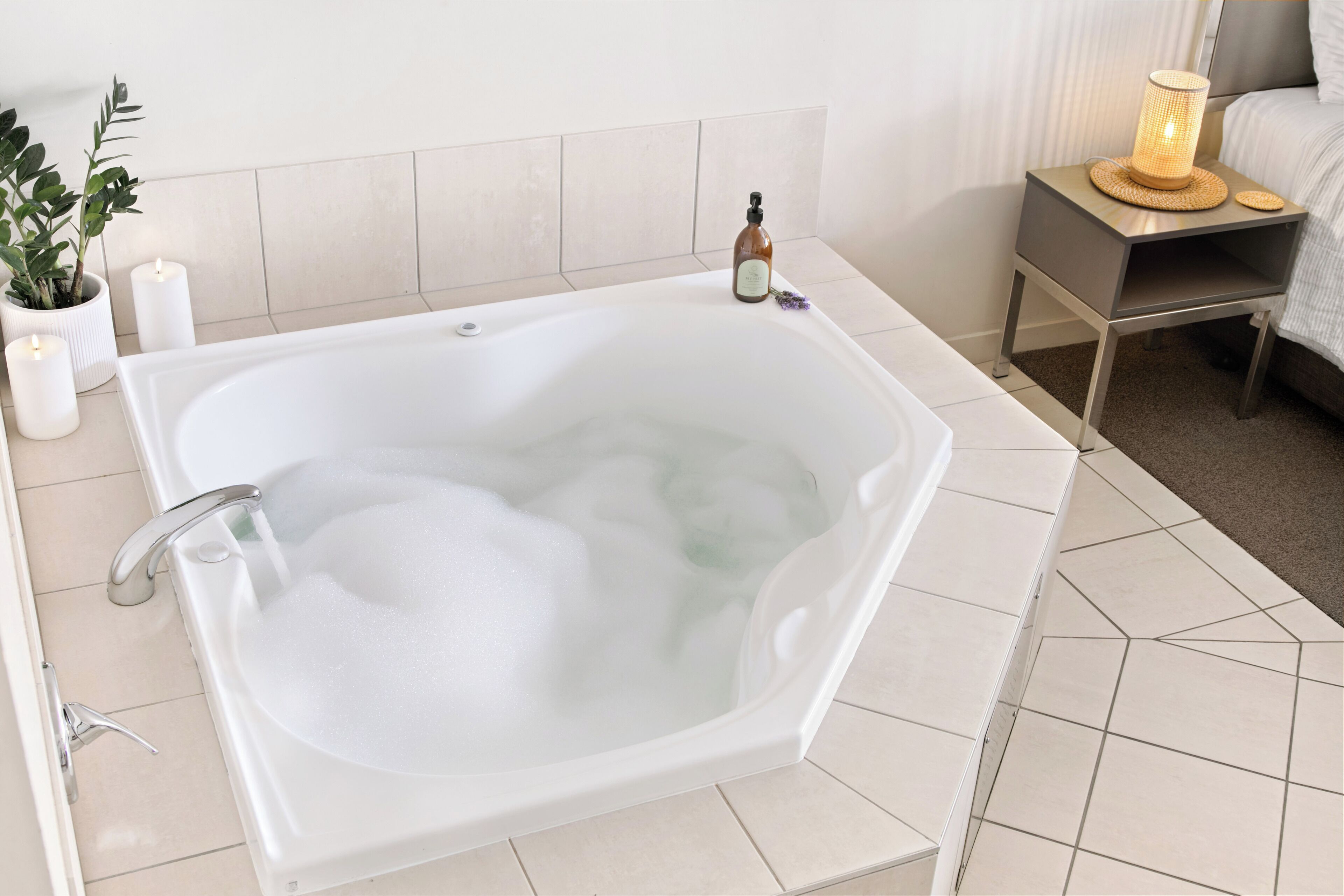 Ein modernes Badezimmer mit freistehender Badewanne, einem Nachttisch mit Lampe und einem Blumentopf.