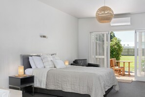 A bedroom with a bed, bedside tables, a hanging light fixture, and a view of the outdoors through a sliding glass door. - Ocean Beach Wainui (Gisborne)