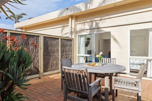 A patio with a round table and wooden chairs, a woven fence, and tropical plants. - Ocean Beach Wainui (Gisborne)