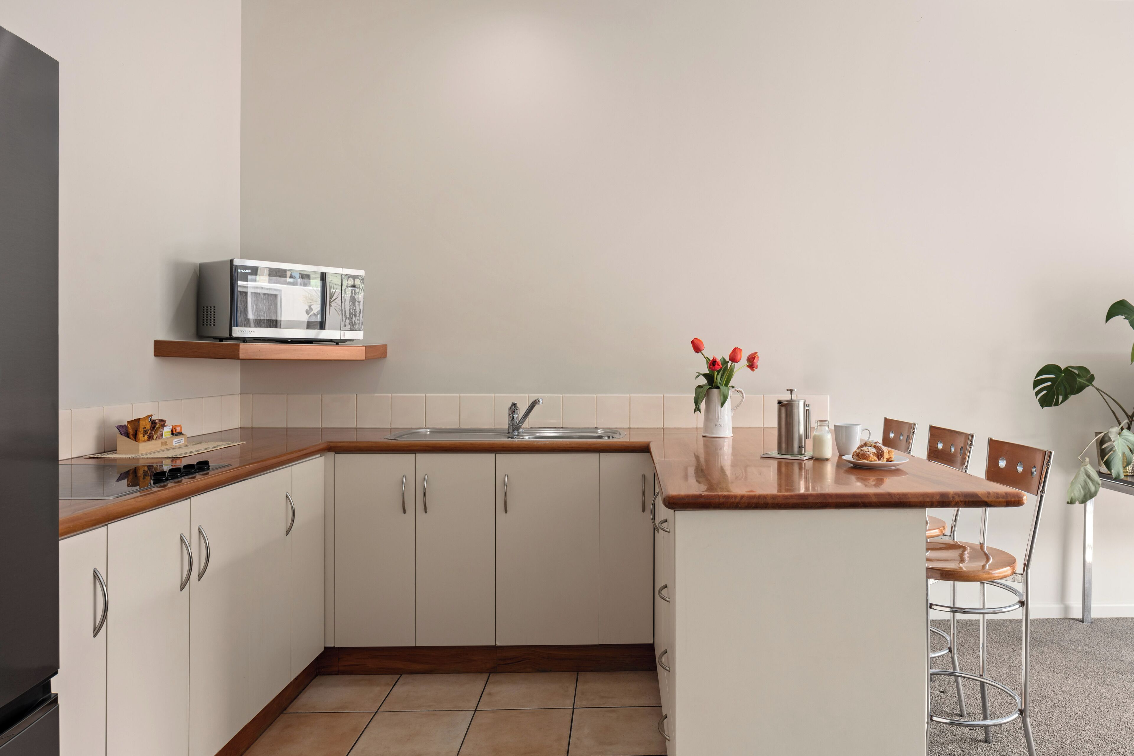 A modern kitchen with white cabinets, a wooden countertop, a built-in microwave, and a small dining area with a chair and table.