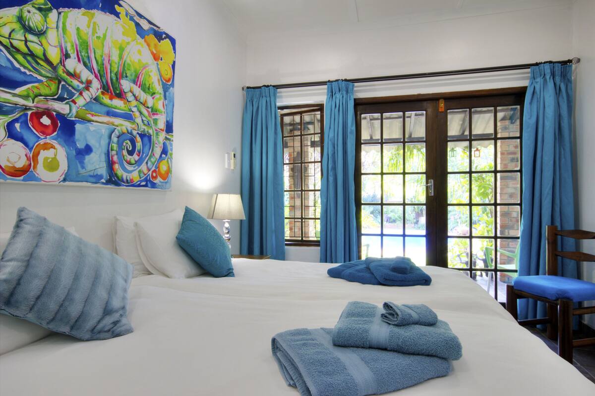 A hotel room with a large bed, two pillows, a blue chair, and a painting on the wall.