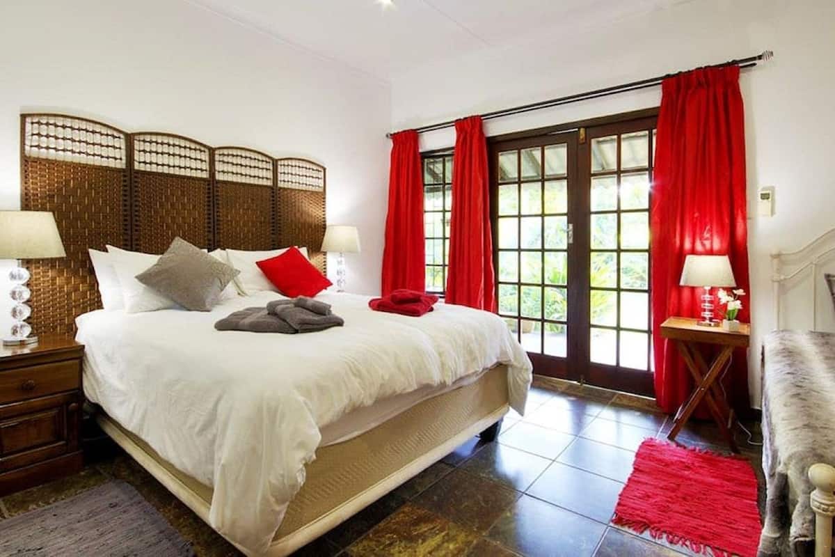 A spacious bedroom with a large bed, a wooden headboard, and a view through a glass door.