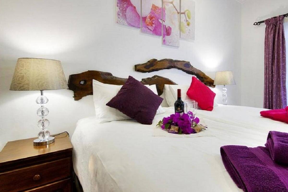 A hotel room with a wooden headboard, white bedding, a bedside table with a lamp, and artwork on the wall.