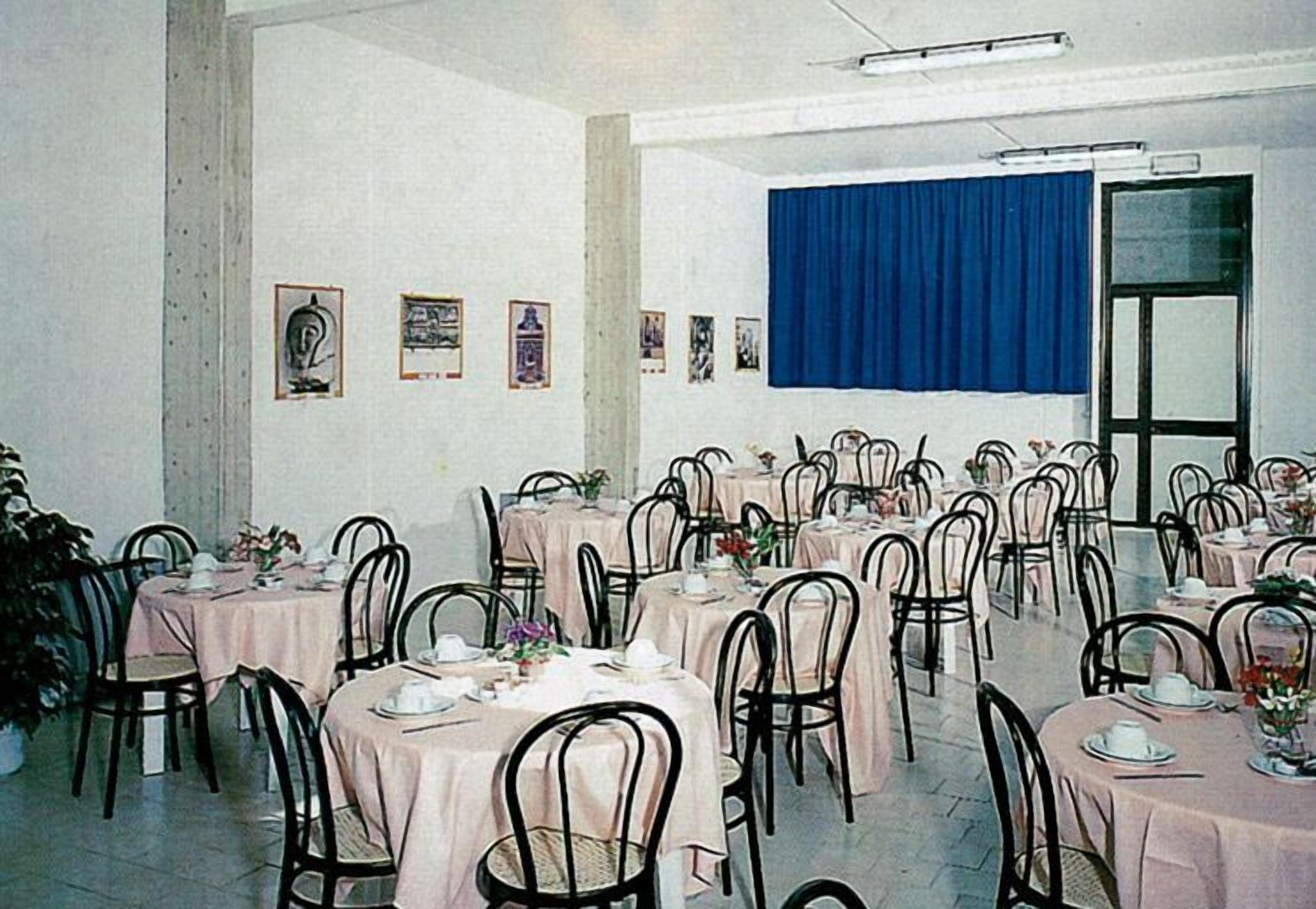 Ein Festsaal mit mehreren runden Tischen, die mit rosa Tischdecken bedeckt sind, schwarzen Stühlen und gerahmten Bildern an den Wänden.