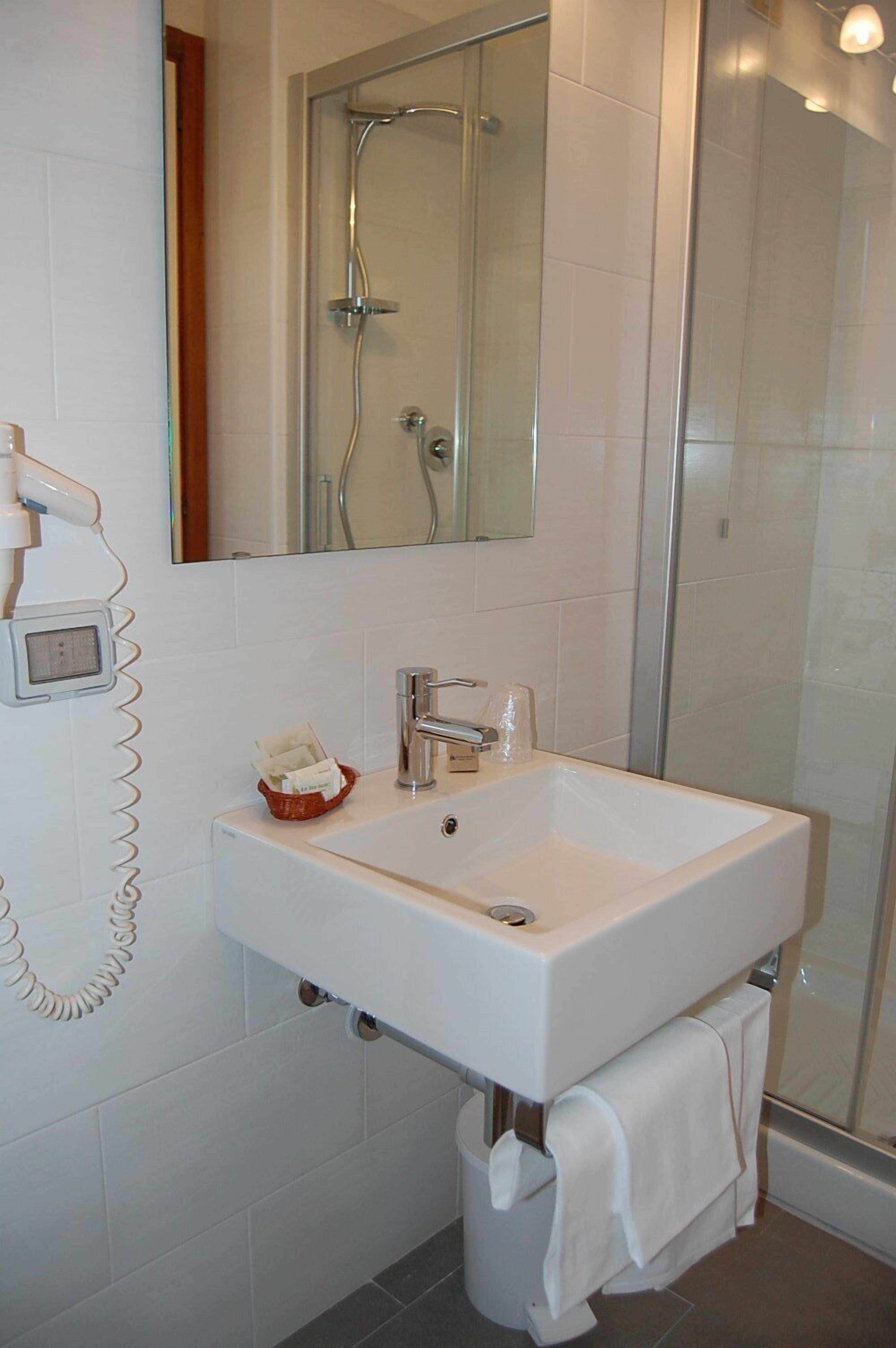 Une salle de bain avec un lavabo blanc, un miroir, une cabine de douche en verre et un porte-serviettes.