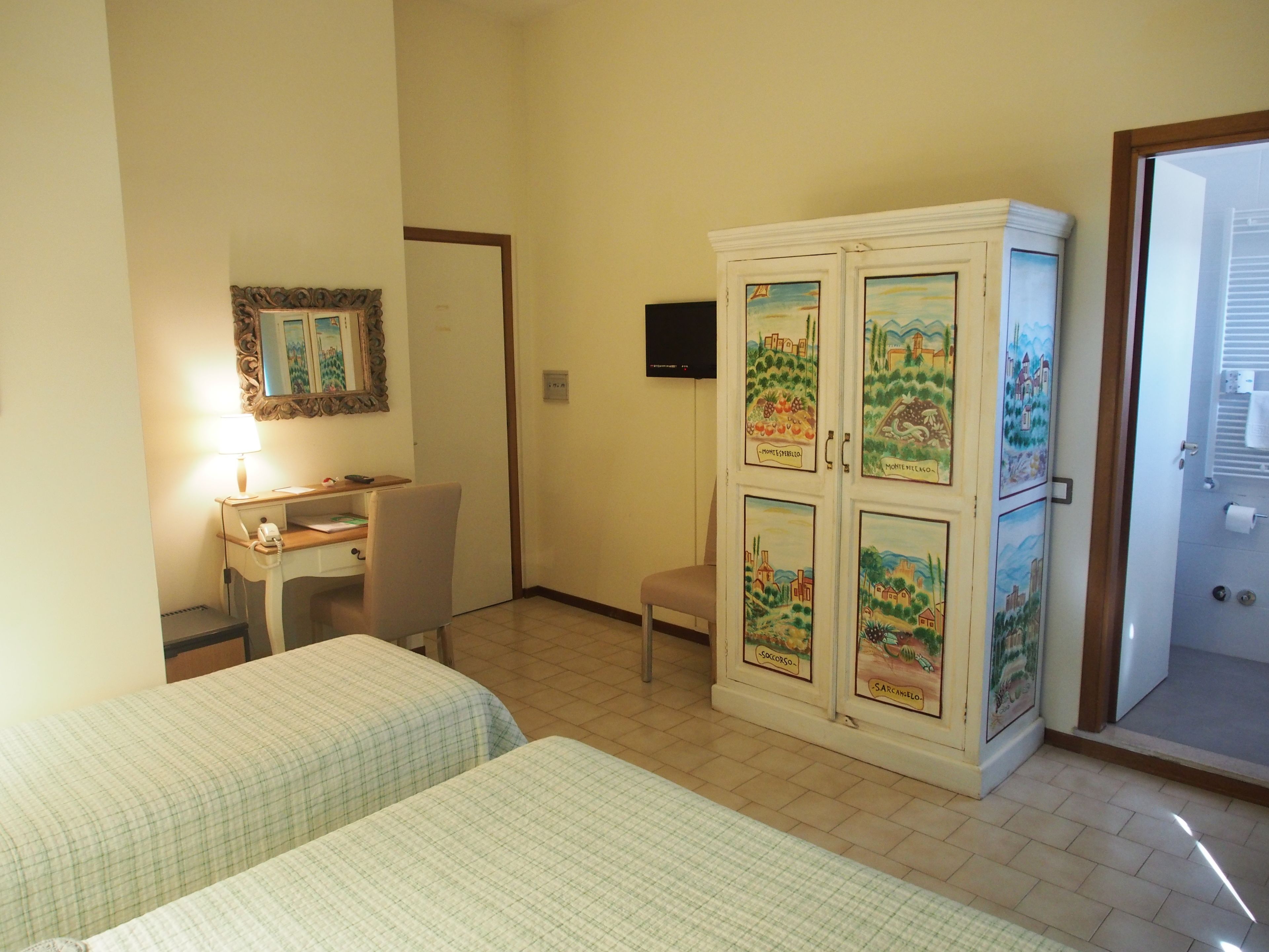 A hotel room with two beds, a desk, a chair, a cabinet with artwork, and a television.