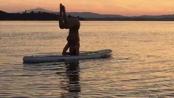 Eine Person steht auf einem Stand-Up-Paddleboard auf dem Wasser bei Sonnenuntergang.