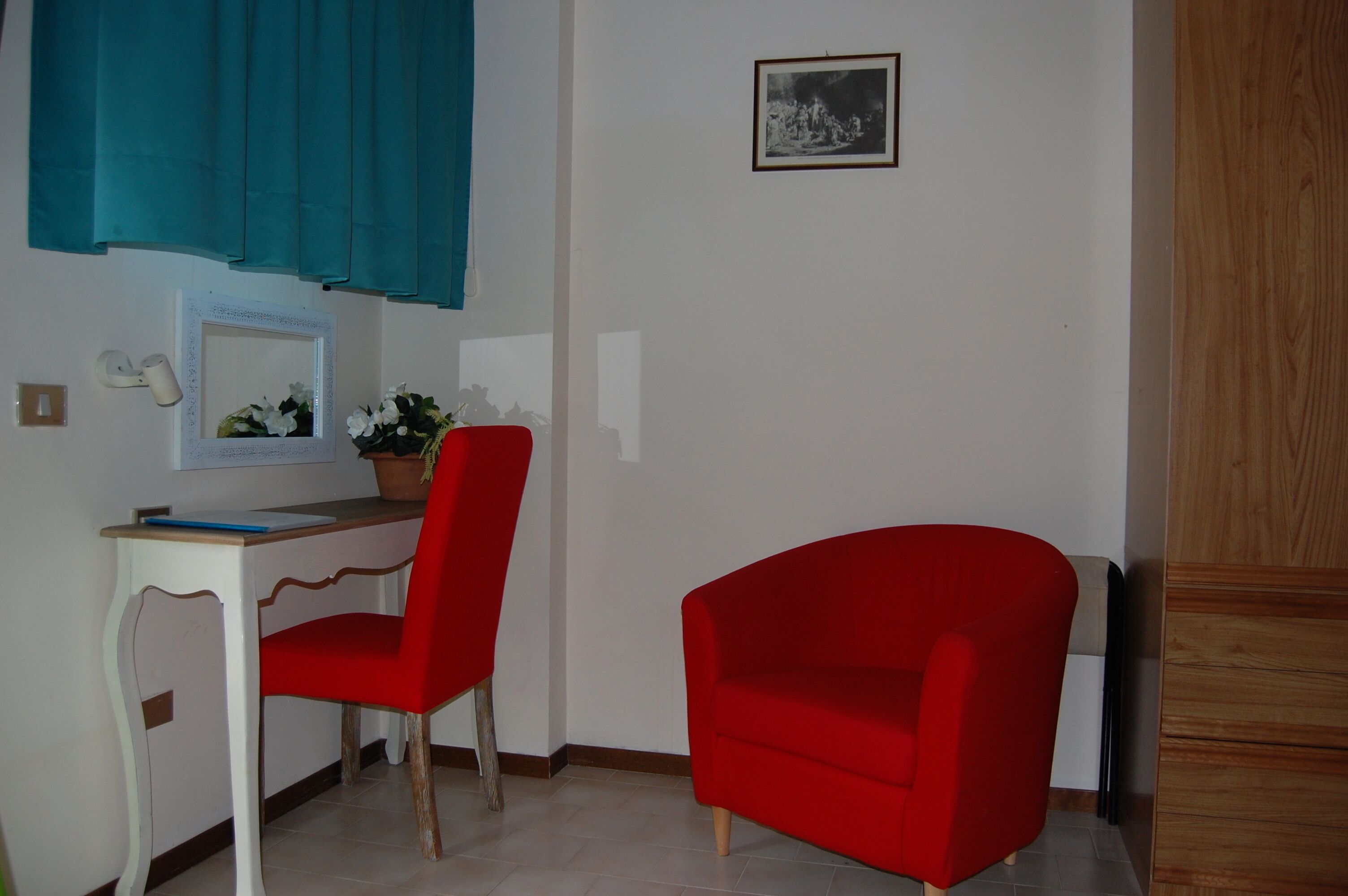 A room with a desk, a red chair, a potted plant, and a framed picture on the wall.