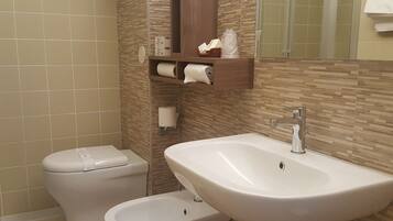 Ein Badezimmer mit Toilette, Bidet und Waschbecken. Handtücher und Pflegeprodukte sind an der Wand angebracht.