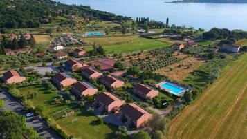 Residential homes with red-tiled roofs are nestled among well-manicured lawns and gardens, near a large body of water.