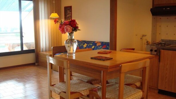 A dining area with a wooden table and chairs, a vase with flowers, and a window with curtains. - Le Tre Isole (Magione)
