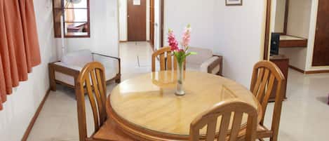 A dining area with a round wooden table, four wooden chairs, a vase with flowers, a sofa, and a mirror on the wall.
