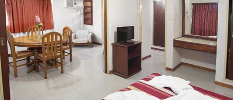 A hotel room with a bed, a desk with chairs, a television, and a window with curtains.