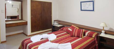 A hotel room with a bed, a wooden wardrobe, a bedside table with a lamp, and a mirror.