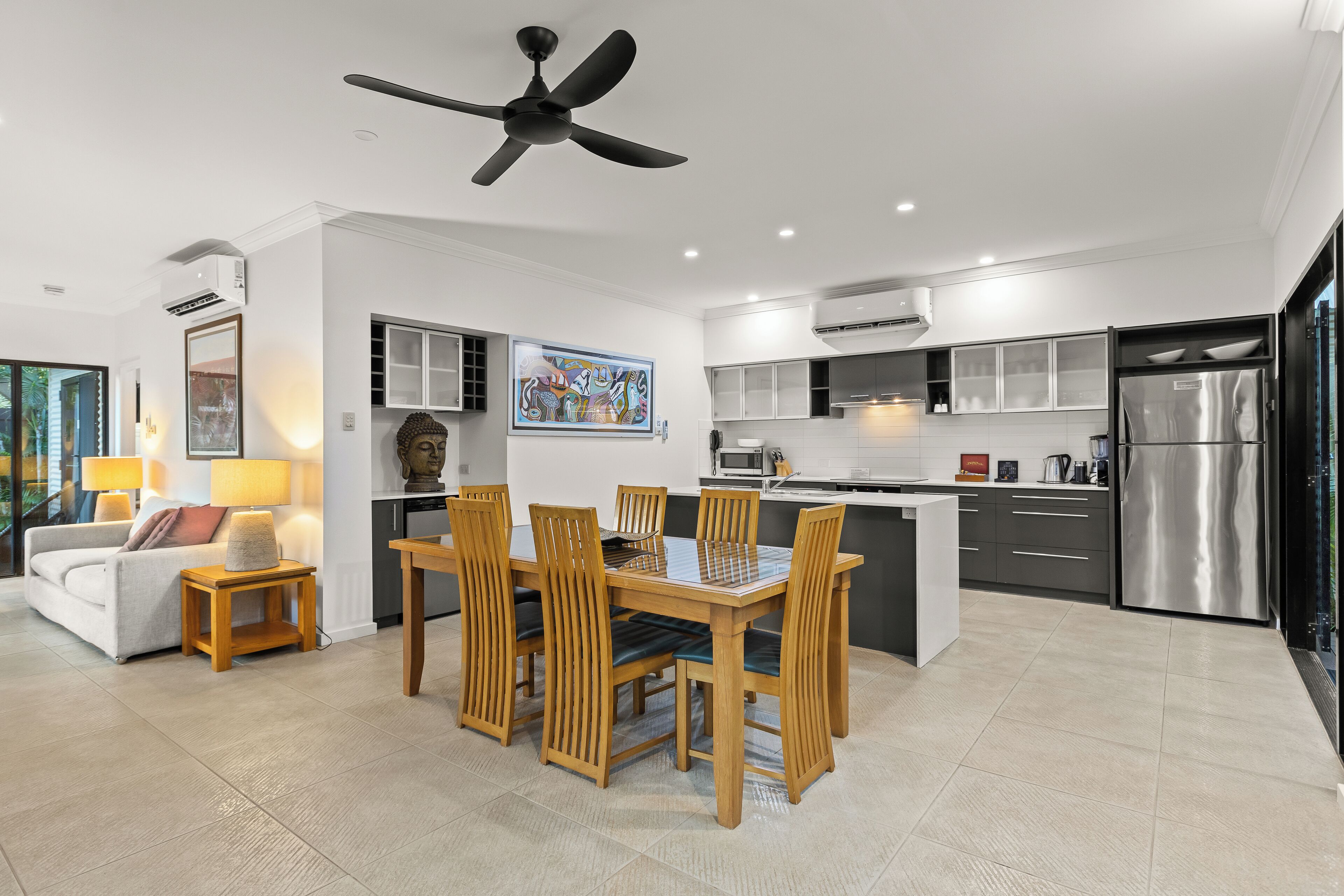 A modern kitchen with a central island, built-in appliances, and a dining area with wooden furniture.
