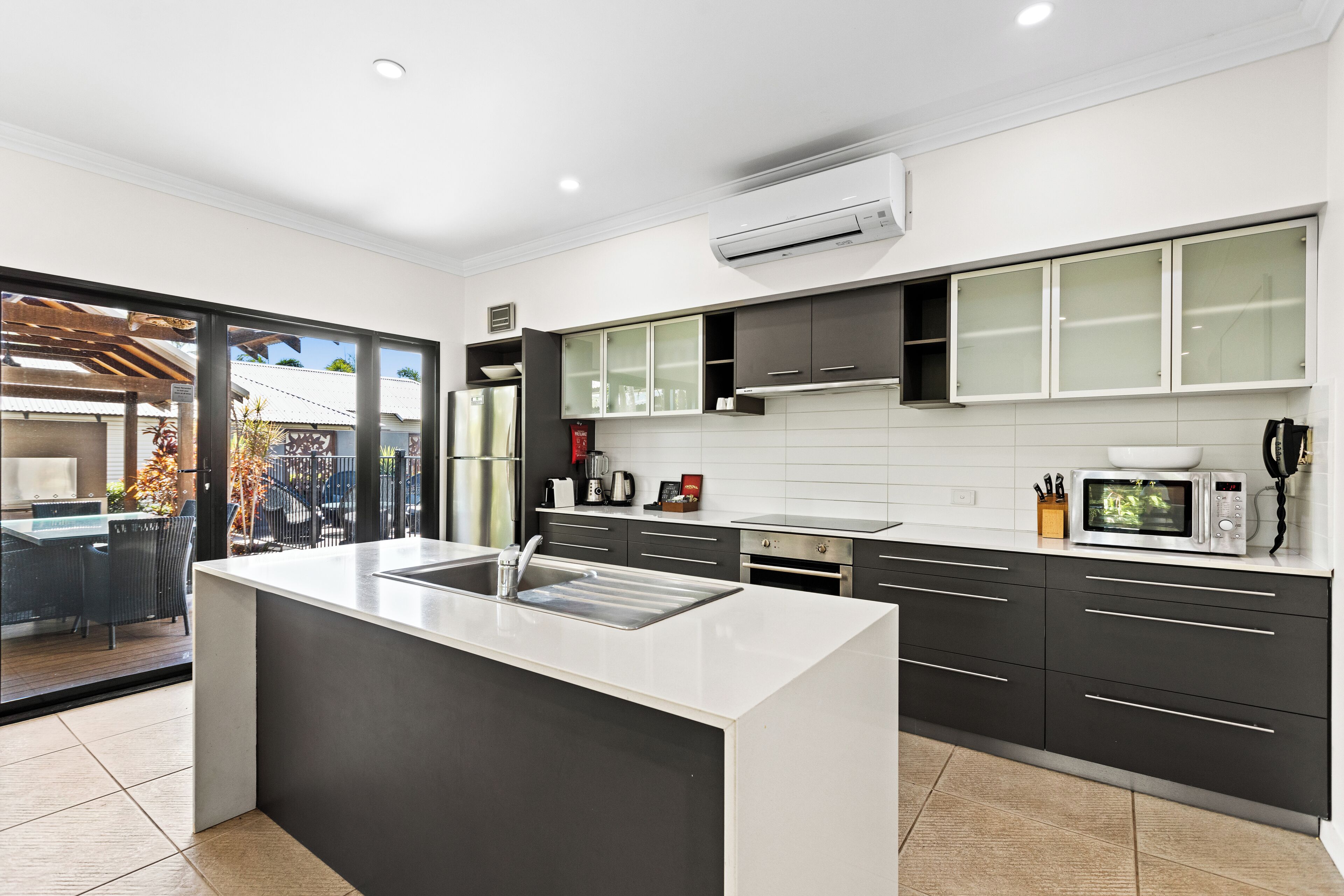 Una cocina moderna con una isla central, muebles oscuros y un ventanal grande.