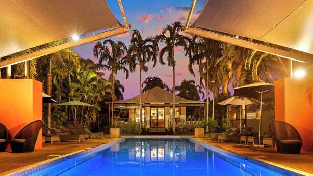 A poolside area with lounge chairs, umbrellas, and a building with a sign.
