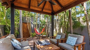 A wooden deck with outdoor furniture, a hammock, and lush tropical plants.
