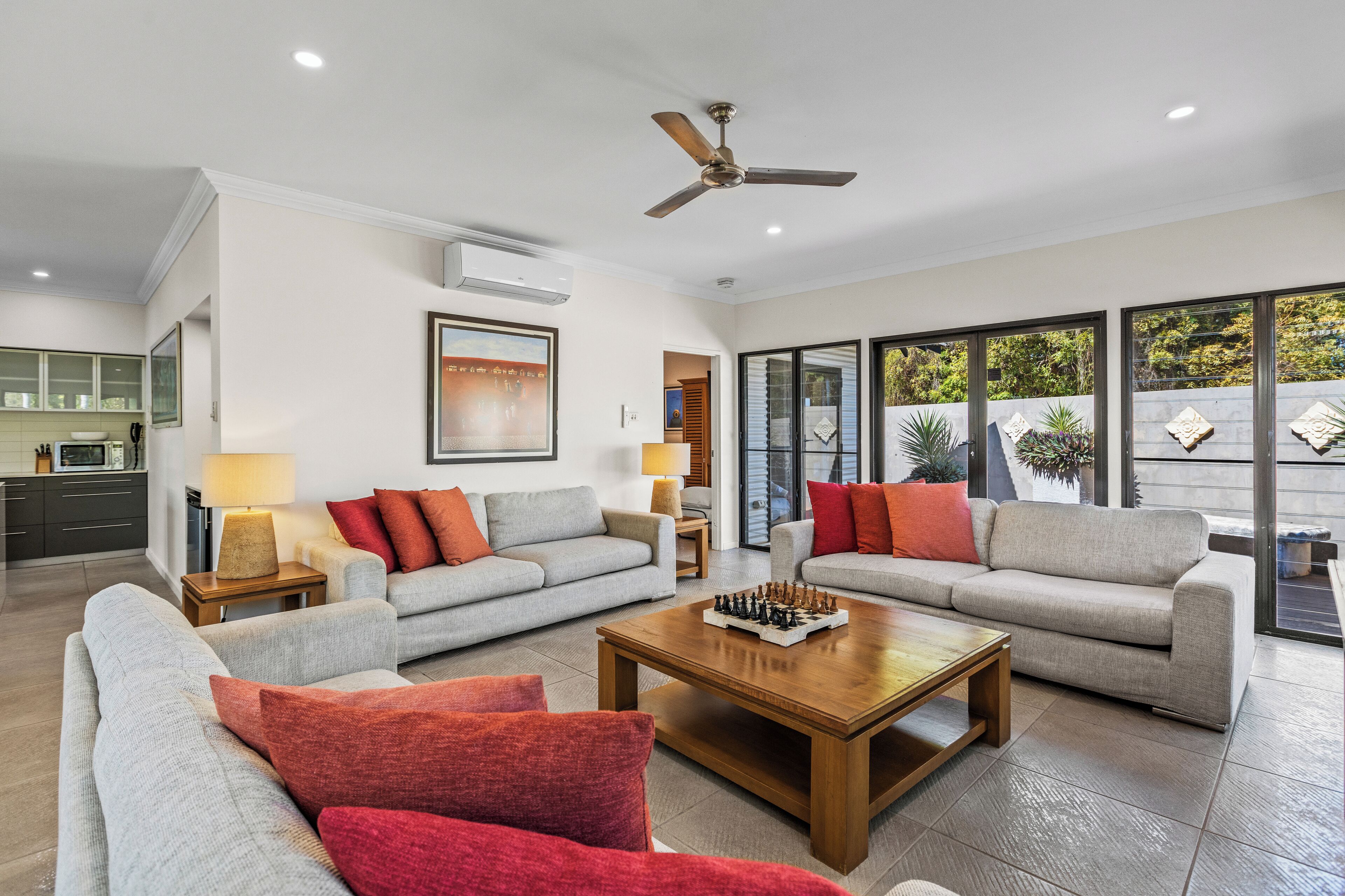 A spacious living room with two grey sofas, red cushions, a wooden coffee table, and a ceiling fan.
